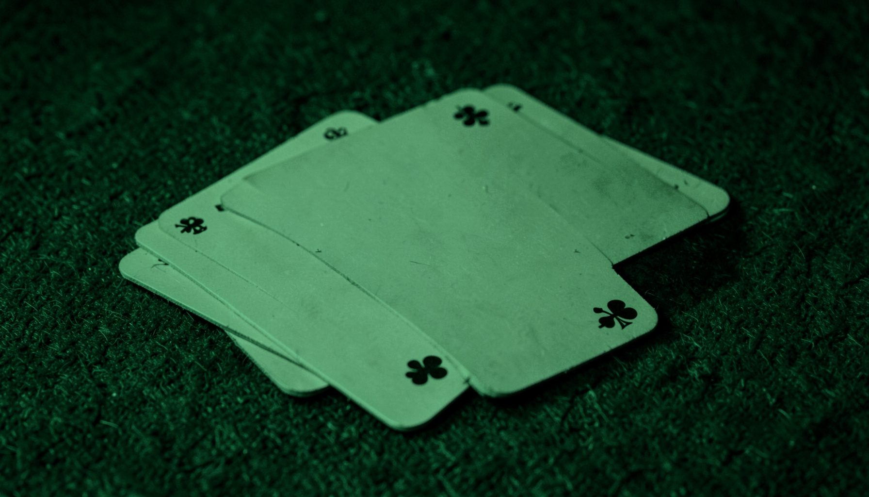 Two-tone dark green duotone photograph of overlapping playing cards on a felt surface, with deep emerald shadows and muted lime highlights, calm and understated mood